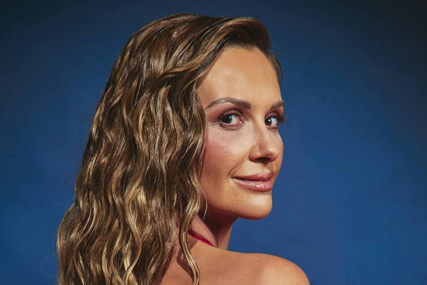 Carly Pearce turns and smiles in front of a blue backdrop.