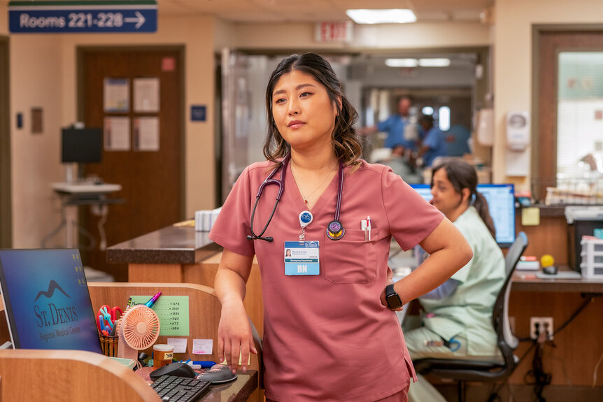 Serena stands with her hand on her hip leaning on a desk on St. Denis Medical Season 1 Episode 1