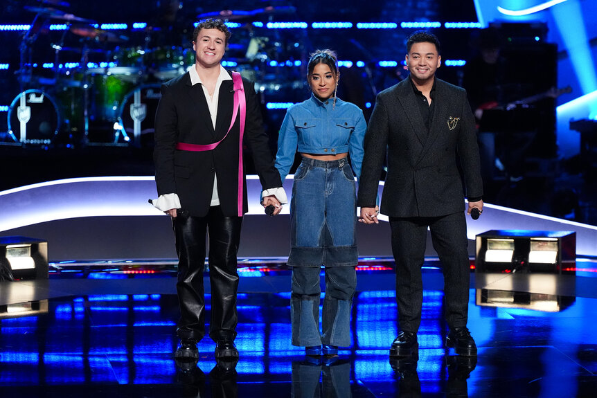 Jeremy Beloate, Kiara Vega and Sofronio Vasquez hold hands on stage on The Voice Season 26 Episode 14