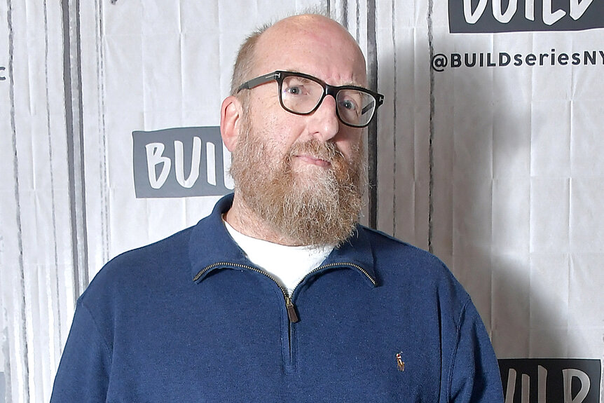 Brian Posehn wears a blue shirt and glasses at aol build studio