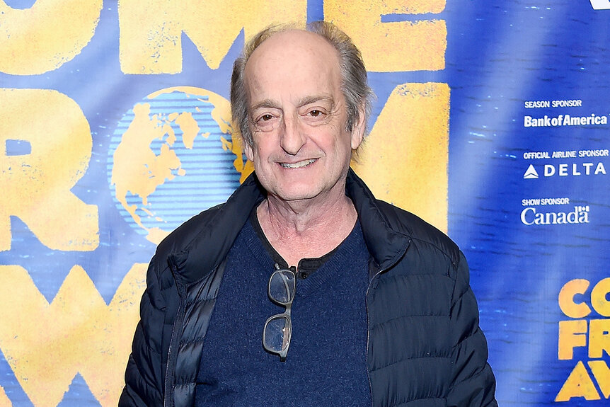 David Paymer smiles in a blue shirt and black jacket on the red carpet