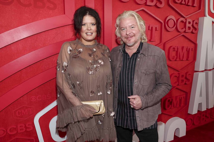 Rebecca Arthur and Phillip Sweet smile together in front of a red backdrop.