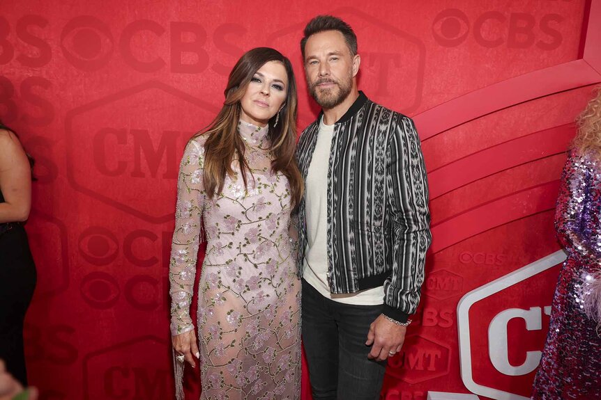 Karen Fairchild and Jimi Westbrook pose together in front of a red backdrop.