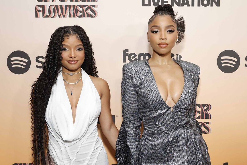 Halle Bailey and Chloe Bailey pose together in white and silver dresses.