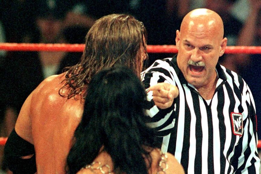 Jesse Ventura points and yells at two wrestlers during a match.