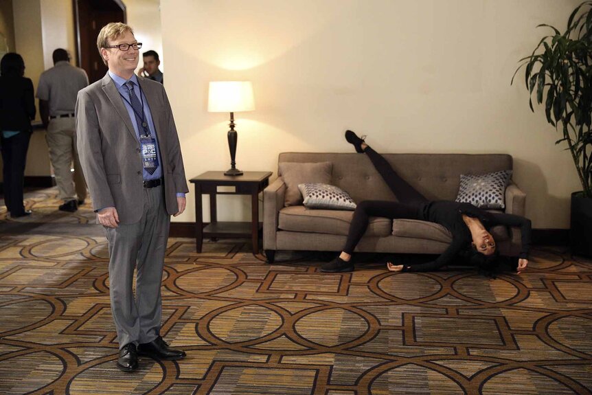 Jeffrey Bouche (Andrew Daly) stands and smile while Rosa Diaz (Stephanie Beatriz) lays on a couch in Brooklyn Nine-Nine Episode 416.