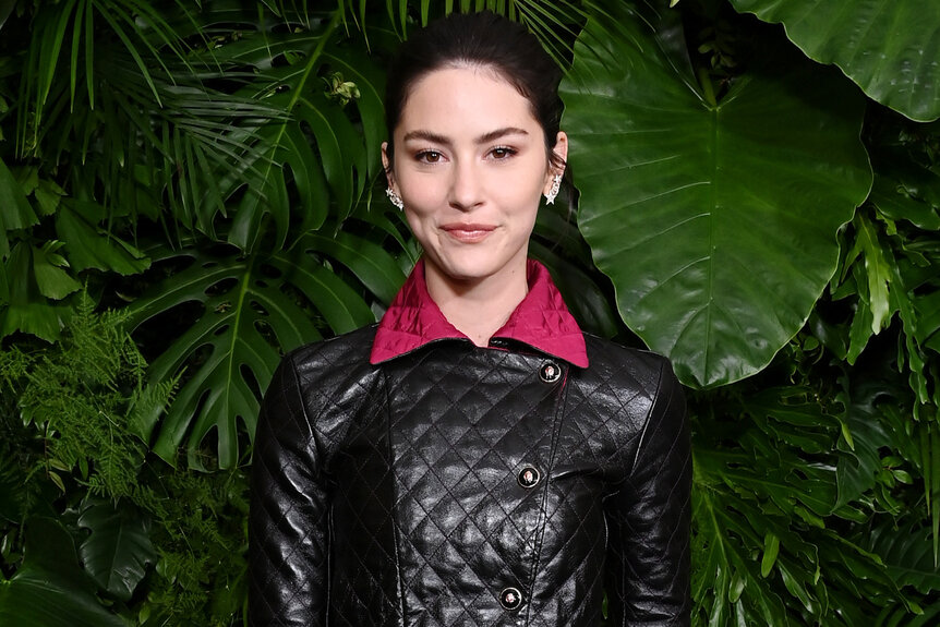 Gracie Abrams wears a leather jacket in front of greenery at HANEL and Charles Finch Annual Pre-Oscar Dinner