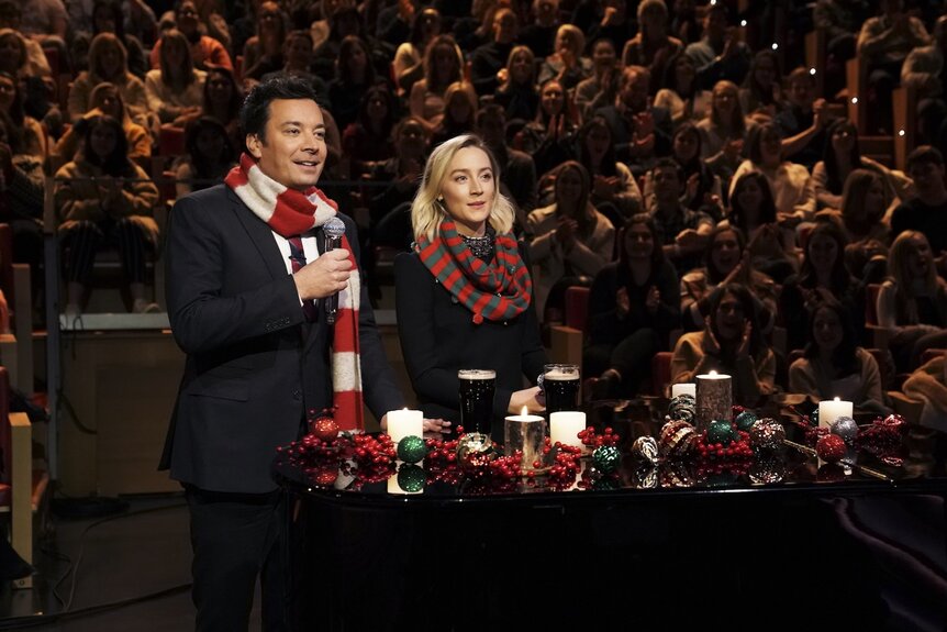 immy Fallon and Saoirse Ronan wear striped Christmas sweaters and stand in front of candles.