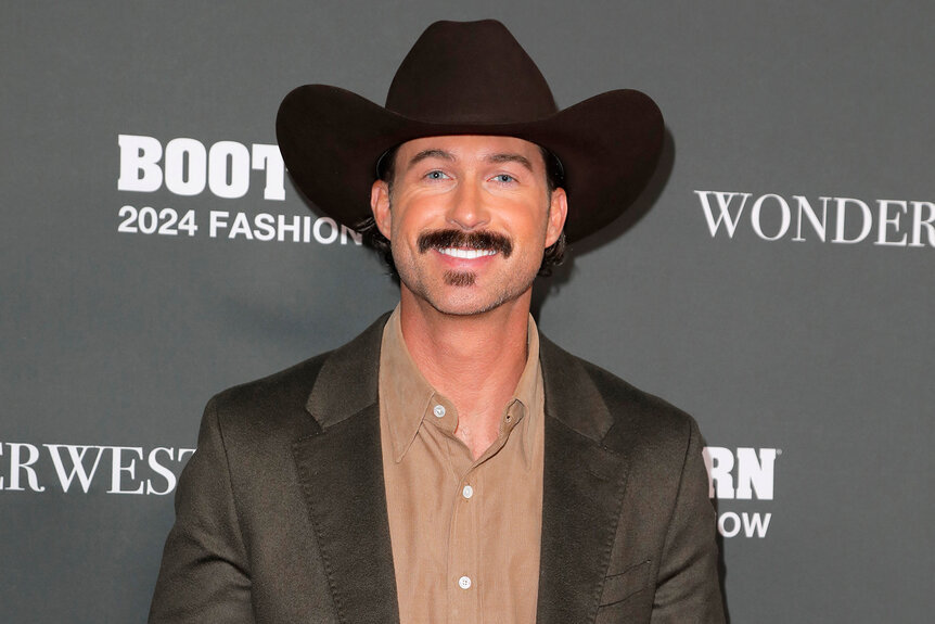 Riley Green wears a grey jacket and cowboy hat on the red carpet