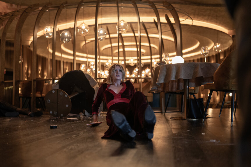 Violet sits on the floor of a restaurant looking scared in the movie Drop