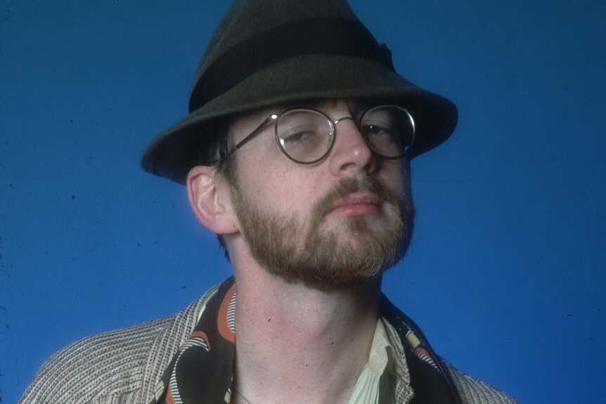 Michael O'Donoghue wears a fedora and silver wire glasses.