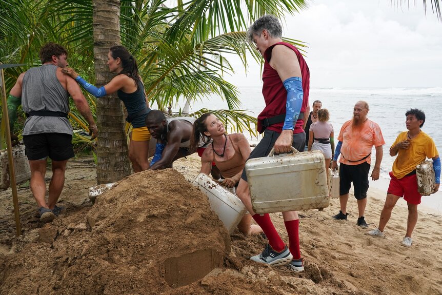 The cast digs through sand together on Deal or No Deal Island Episode 203.